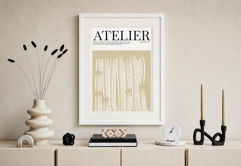 May include: A framed art print with the word "ATELIER" in black. The artwork features vertical white lines on a beige background. A vase with black stems, candles, and decorative objects complete the scene.