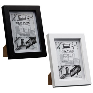May include: Two black and white photo frames with a box frame design. The frames are made of wood and have a simple, modern design. The frames are both 5x7 inches and feature a picture of a New York City street scene with a "Broadway" sign.