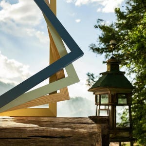 May include: Three picture frames stacked on top of each other. The top frame is a dark blue, the middle frame is a light green, and the bottom frame is a natural wood color. The frames are in focus, and the background is blurred.