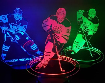May include: Three illuminated hockey player figures with vibrant neon colors. Each figure is a different player, with names and team logos displayed on the base. The players are Sidney Crosby, Connor McDavid, and Leon Draisaitl.
