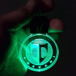 May include: A green glowing keychain with the word "TUSCANI" and a stylized letter "T" inside a circle.