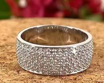 May include: A silver band ring with a wide band and a row of small diamonds set in the metal. The ring is on a wooden surface.