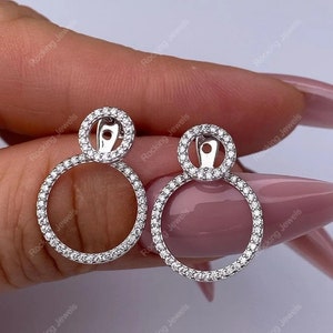 May include: A pair of silver earrings with a double circle design. Each circle is encrusted with small, clear stones.