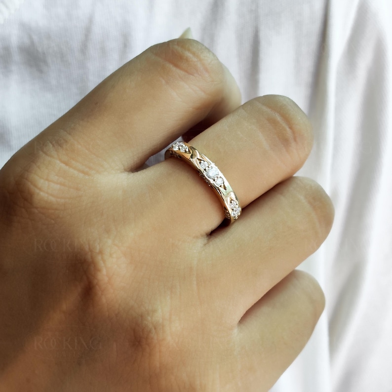 Puede incluir: Un anillo de banda dorada con una serie de peque&ntilde;as piedras claras de corte redondo engastadas en la parte superior. La banda de metal tiene un patr&oacute;n texturizado similar a un tejido que enmarca cada piedra, creando un dise&ntilde;o decorativo continuo.