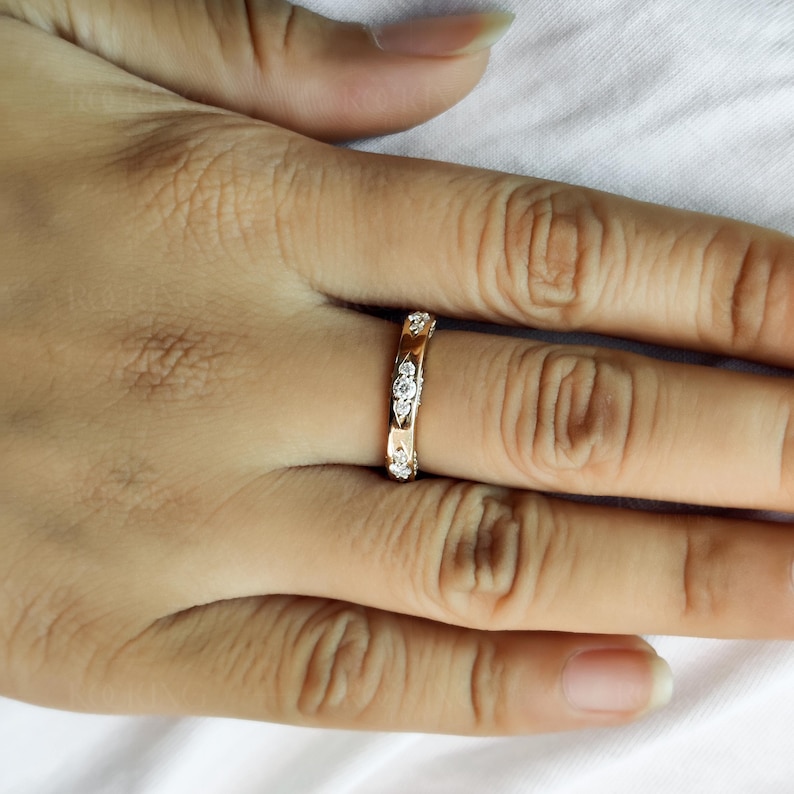 Puede incluir: Un anillo de banda en oro rosa que presenta una serie de peque&ntilde;as piedras claras de corte redondo engastadas en monturas met&aacute;licas individuales con forma de marquesa, dispuestas en un patr&oacute;n repetitivo a lo largo de la superficie exterior.