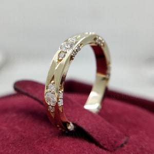 Puede incluir: Un anillo de banda de oro con una serie de piedras redondas, claras y facetadas incrustadas en la superficie met&aacute;lica. El anillo tiene un acabado pulido y un patr&oacute;n geom&eacute;trico repetitivo a lo largo de la banda, con el texto ROCKING JEWELS al fondo.