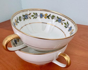 May include: Two white porcelain teacups with gold trim and a blue and yellow floral design. The cups are stacked on top of each other.