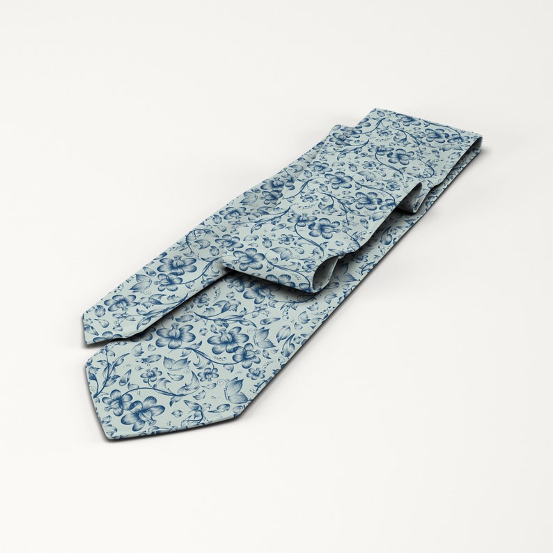 May include: A light blue necktie with a repeating floral pattern in a darker shade of blue. The tie is made of a smooth fabric and is displayed on a white background. The floral design includes stylized flowers and leaves.