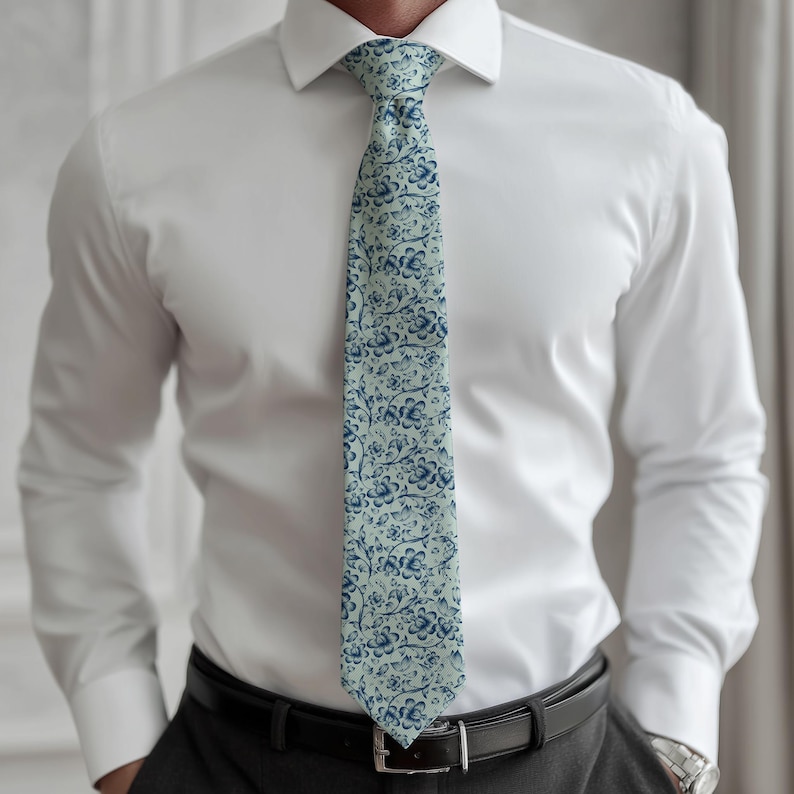 May include: A light blue tie with a repeating floral pattern in navy blue. The tie is worn over a white dress shirt and is secured with a black belt. The floral design is a classic pattern.