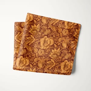 May include: Two folded decorative fabric pieces with a floral pattern. The fabric features a repeating design of large, stylized flowers and foliage in shades of gold and brown. The background is a deep reddish-brown color.