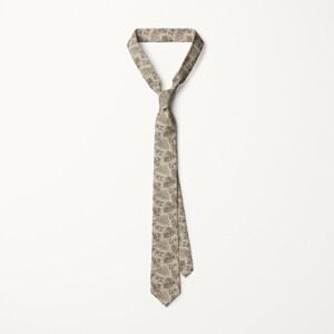 May include: A beige necktie with a repeating pattern of stylized leaves. The tie is knotted at the top and hangs vertically against a white background. The leaf pattern is in shades of brown and tan.