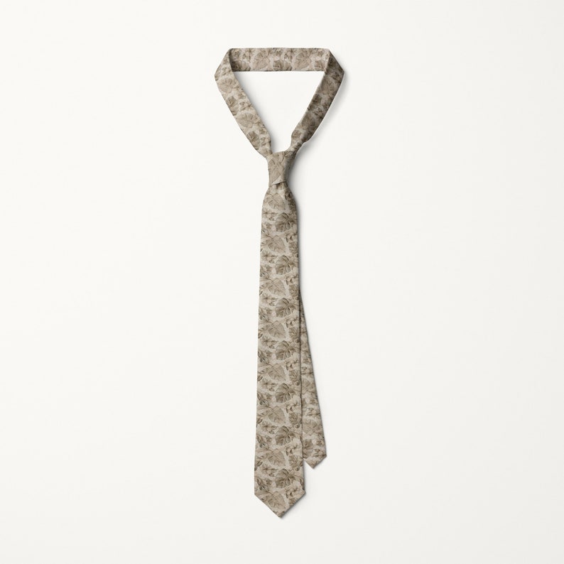 May include: A beige necktie with a repeating pattern of stylized leaves. The tie is knotted at the top and hangs vertically against a white background. The leaf pattern is in shades of brown and tan.