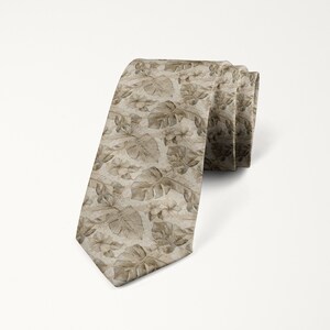 May include: A rolled-up necktie featuring a repeating pattern of beige-colored tropical leaves and flowers. The tie is a neutral color, with a subtle sheen, and is suitable for formal or semi-formal occasions.