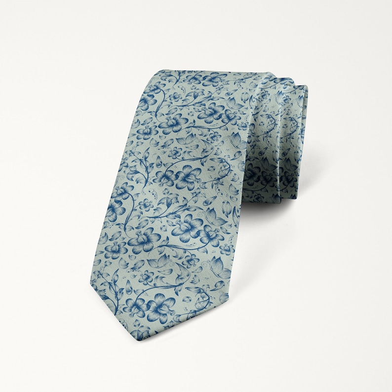 May include: A rolled-up necktie with a floral pattern. The tie features a light blue background with a repeating design of dark blue flowers and vines. The tie is made of a smooth fabric and is suitable for formal or business attire.