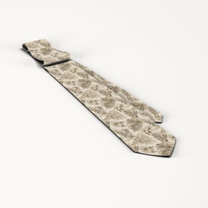 May include: A beige necktie featuring a repeating pattern of tropical leaves and flowers. The tie is made of a light-colored fabric and has a classic pointed end. The design includes various shades of brown and tan.