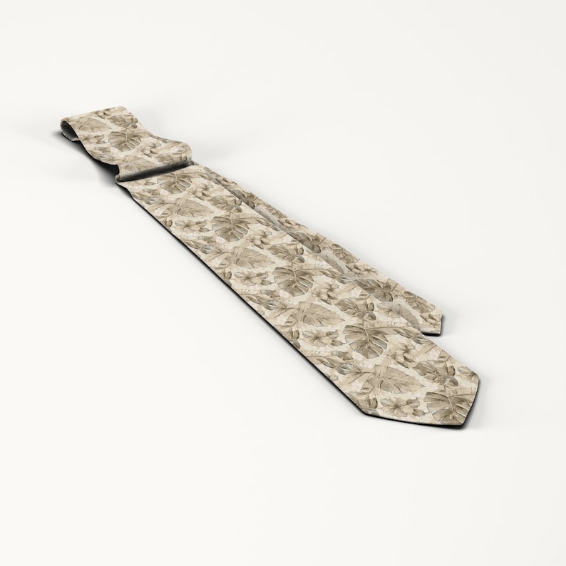 May include: A beige necktie featuring a repeating pattern of tropical leaves and flowers. The tie is made of a light-colored fabric and has a classic pointed end. The design includes various shades of brown and tan.