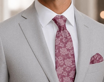 May include: A light gray blazer worn over a crisp white collared shirt, paired with a mauve necktie featuring a detailed floral pattern and a matching pocket square tucked into the breast pocket of the jacket, creating a formal ensemble.