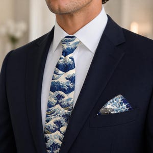 May include: A navy blue suit with a white dress shirt. The tie and pocket square feature a blue and white wave pattern. The tie is centered, and the pocket square is in the suit's breast pocket.