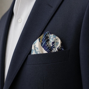 May include: A navy blue blazer with a white dress shirt and a pocket square. The pocket square features a blue and white wave pattern design. The blazer is made of a textured fabric.