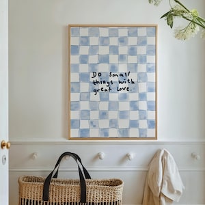 Puede incluir: Una obra de arte enmarcada con un patrón de cuadros azules y blancos y el texto escrito a mano: "Do small things with great love". La obra de arte se exhibe en un pasillo luminoso, con una cesta tejida y un perchero.