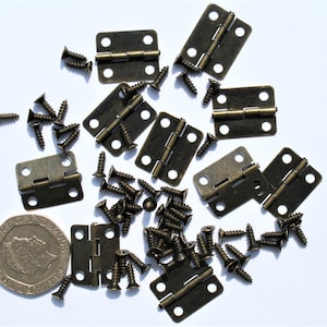 May include: An assortment of small, antique brass-finish hinges and screws scattered on a white background. The hinges are rectangular with rounded corners and two screw holes. A coin is included for size reference.