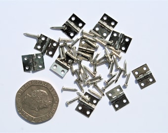 May include: A collection of small, silver-colored hinges and matching screws, scattered on a white surface. A United Kingdom twenty pence coin is included for size comparison. The hinges are approximately 0.75 inches wide when open, and the screws are about 0.5 inches long.