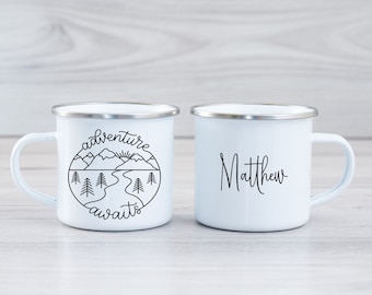 May include: Two white enamel mugs with silver rims. One mug has a black and white illustration of mountains, a river, and trees with the text "adventure awaits". The other mug has the name "Matthew" written in black cursive.