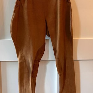 May include: Brown riding pants with a high waist and button details. The pants have reinforced patches on the inner thighs and a tailored fit. The fabric appears to be a sturdy, textured material.