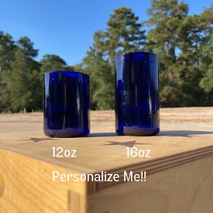 Puede incluir: Dos botellas de vidrio azul, una etiquetada con 12oz y la otra con 16oz, sentadas en una caja de madera con el texto "¡Personalízame!"