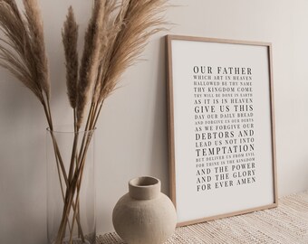 May include: A framed print with the Lord's Prayer in black text on a white background. The print is hanging on a wall with dried pampas grass in a clear vase and a beige ceramic vase on a white woven rug.