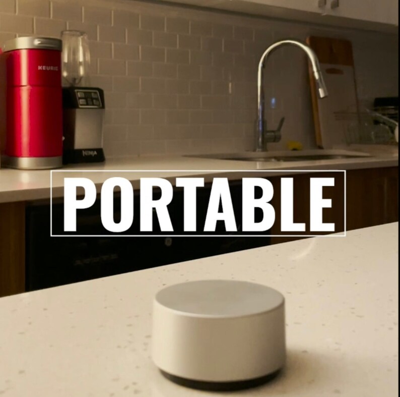 Op de afbeelding: Een ronde, draagbare zilveren luidspreker op een wit aanrecht. Het woord "PORTABLE" staat in witte letters op een zwarte achtergrond boven de luidspreker.