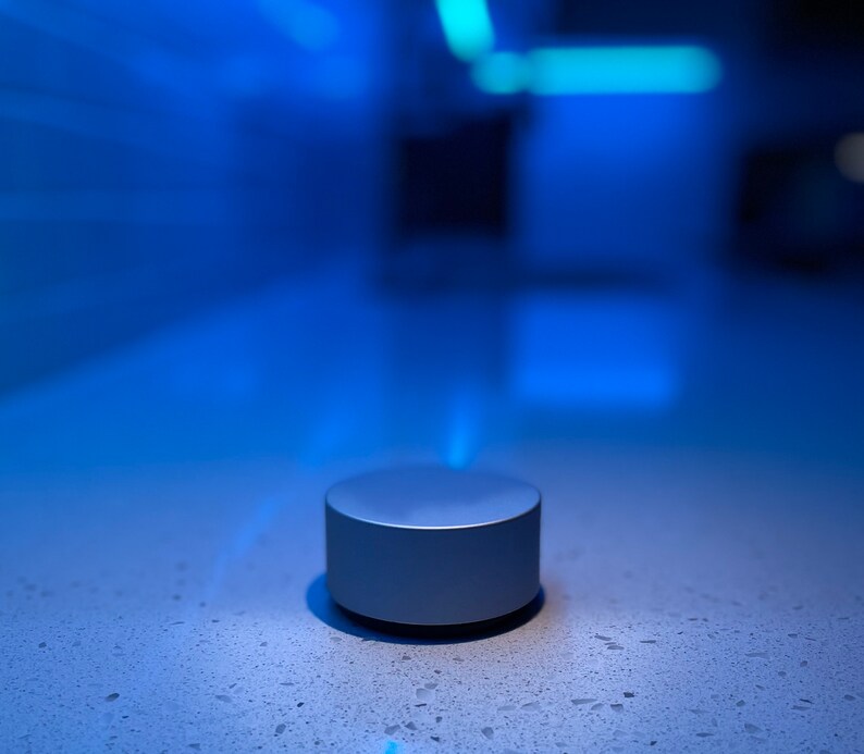 Op de afbeelding: Een ronde zilveren knop met een glad oppervlak op een wit aanrecht met een blauw-wit gevlekt patroon.