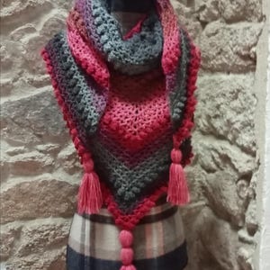 Peut inclure: Un châle triangulaire en crochet de couleur rose, gris et violet. Le châle a une bordure en franges et est présenté sur un mannequin. Le texte "Breizhlaine" est visible sur l'image.