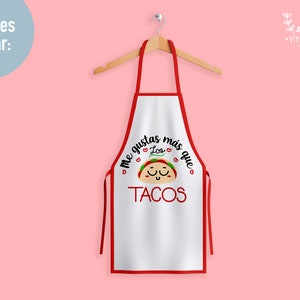 May include: White apron with red trim featuring a cartoon taco with a smiling face and the text "Me gustas m&aacute;s que los tacos".