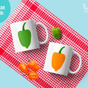 May include: Two white mugs with a red and white checkered tablecloth. One mug has a green pepper illustration and the other has an orange pepper illustration. There are three small orange peppers on the tablecloth.