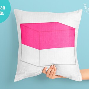May include: A white pillow with a pink and white geometric design. The design is a cube with a pink top and white bottom.