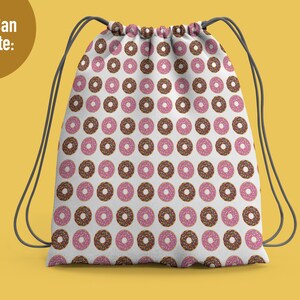 May include: A white drawstring backpack featuring a repeating pattern of donuts with pink frosting and multi-colored sprinkles, along with chocolate frosted donuts with sprinkles. The bag has dark gray cord straps and the text You Can Create.