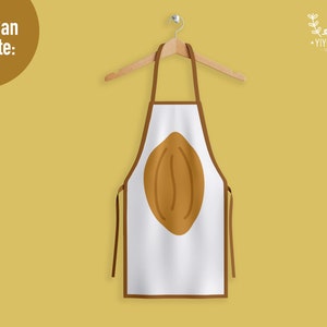 May include: A white apron with brown trim and a large brown coffee bean graphic centered on the front. The apron hangs from a wooden hanger against a solid mustard yellow background. The text "You Can Create:" appears in the top left corner.