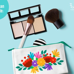 May include: A white zippered pouch with a green zipper pull. The pouch has a colorful floral design with red, yellow, orange, green, purple, and pink flowers. The pouch is on a light blue background with a makeup brush, a makeup palette, and a small black and white striped circle.