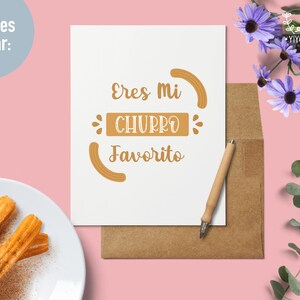 May include: A white card with the text "Eres mi Churro Favorito" in brown lettering. The card is on a brown envelope with a white background. There are churros on a white plate in the lower left corner of the image.
