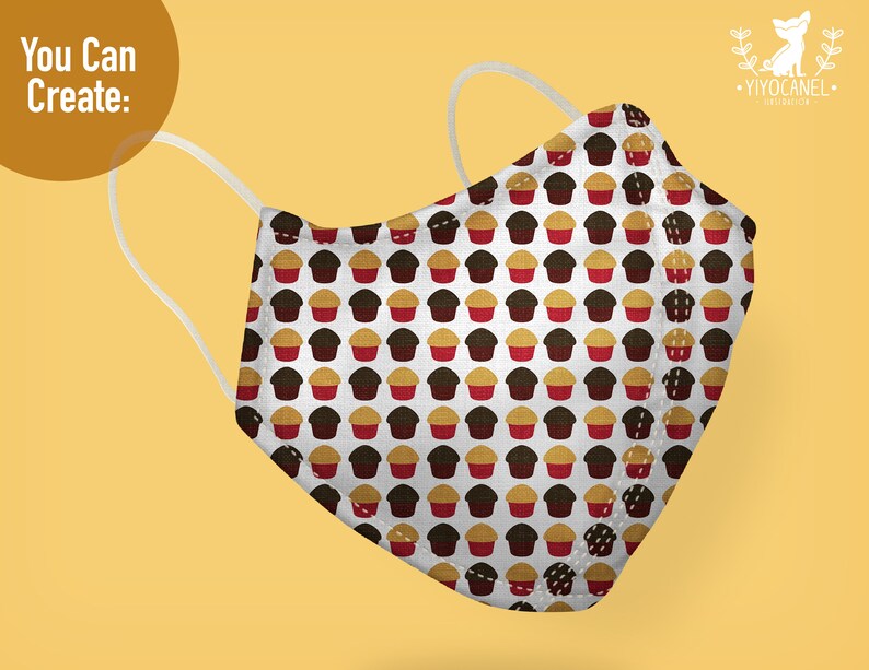 May include: A white face mask featuring a repeating pattern of small brown and red cupcakes. The mask has two white elastic ear loops and a structured, pointed front seam. The text "You Can Create:" appears in the upper left corner of the image.