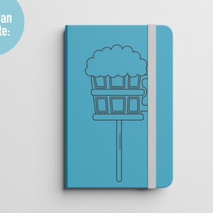 K&ouml;nnte beinhalten: Ein blaues Notizbuch mit einem wei&szlig;en Gummibandverschluss. Das Notizbuch zeigt eine schwarze Linienzeichnung eines Bierkruges mit Schaumkrone.