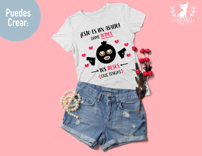May include: A white t-shirt with a black and white illustration of a masked figure holding a gun. The text on the shirt reads "JESTO ES UN ASALTO! DAME TODOS LOS BESOS QUE TENGAS".