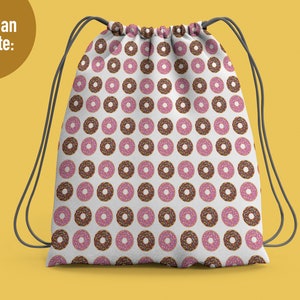 May include: A white drawstring backpack featuring a repeating pattern of donuts with pink frosting and multi-colored sprinkles, along with chocolate frosted donuts with sprinkles. The bag has dark gray cord straps and the text You Can Create.