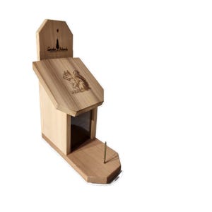 May include: A wooden birdhouse with a pitched roof and a small porch. The roof features an engraved image of a squirrel. The birdhouse has a rectangular body and a small hole for entry. The text "Garden Friends" is visible on the top.