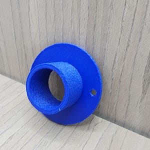 Può includere: Un oggetto blu brillante, stampato in 3D, con una base circolare e un'apertura cilindrica. L'oggetto presenta un piccolo foro laterale e una superficie strutturata. Il design suggerisce un raccordo o un connettore per varie applicazioni.