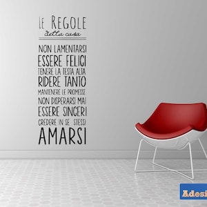 Puede incluir: Una pared blanca con texto negro que dice "LE REGOLE della casa" seguido de una lista de reglas en italiano: "NON LAMENTARSI ESSERE FELICI TENERE LA TESTA ALTA RIDERE TANTO MANTENERE LE PROMESSE NON DISPERARSI MAI ESSERE SINCERI CREDERE IN SE STESSI AMARSI". Una silla roja con patas blancas está en la esquina inferior derecha de la imagen.