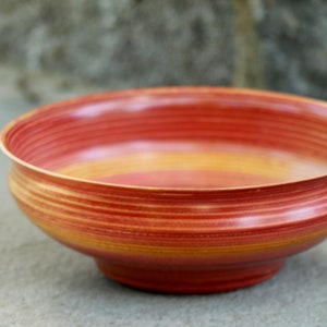 May include: A red and orange wooden bowl with a striated pattern. The bowl is round and has a wide base.
