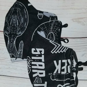 May include: Two black fabric face masks with a white print of the Star Trek logo and starships. The masks have black elastic ear loops and a black adjustable nose wire.