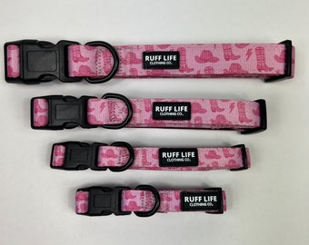 Może przedstawiać: Cztery różowe obroże dla psa z czarną klamrą i czarną etykietą z napisem "RUFF LIFE CLOTHING CO.". Obroże mają różowo-biały wzór kowbojskich butów i kapeluszy.